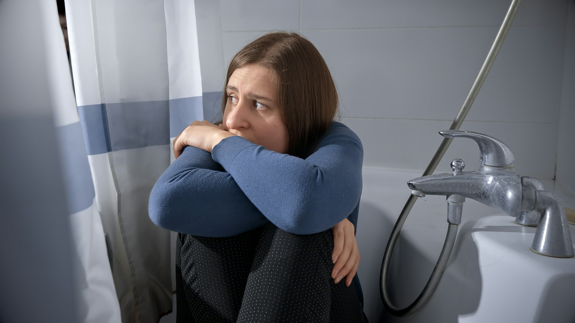 Scared woman being victim of domestic violence and abuse hiding in bath