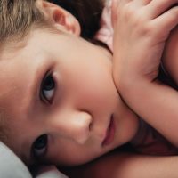 cute, frightened child looking at camera while lying in dark bedroom